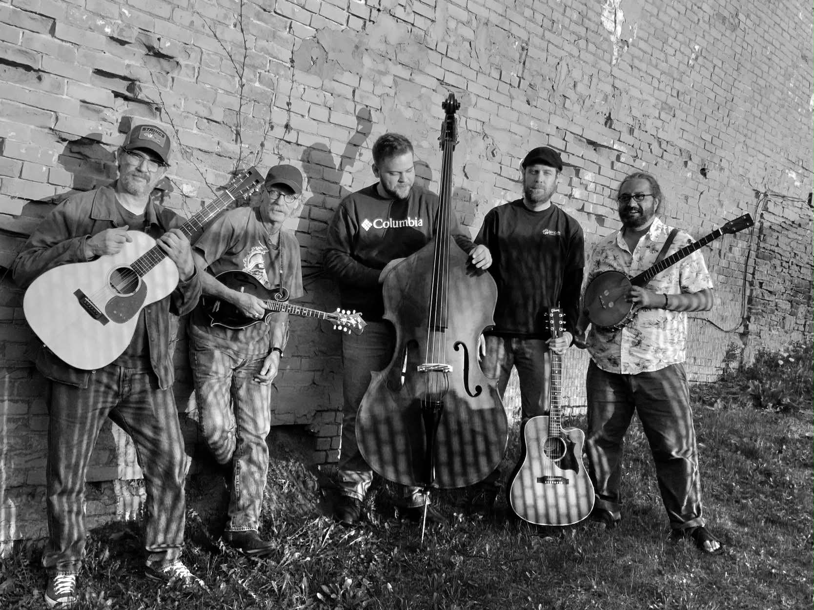 Drifting From Shore — five members posed against a weathered brick wall with guitars, mandolin, banjo, and upright bass